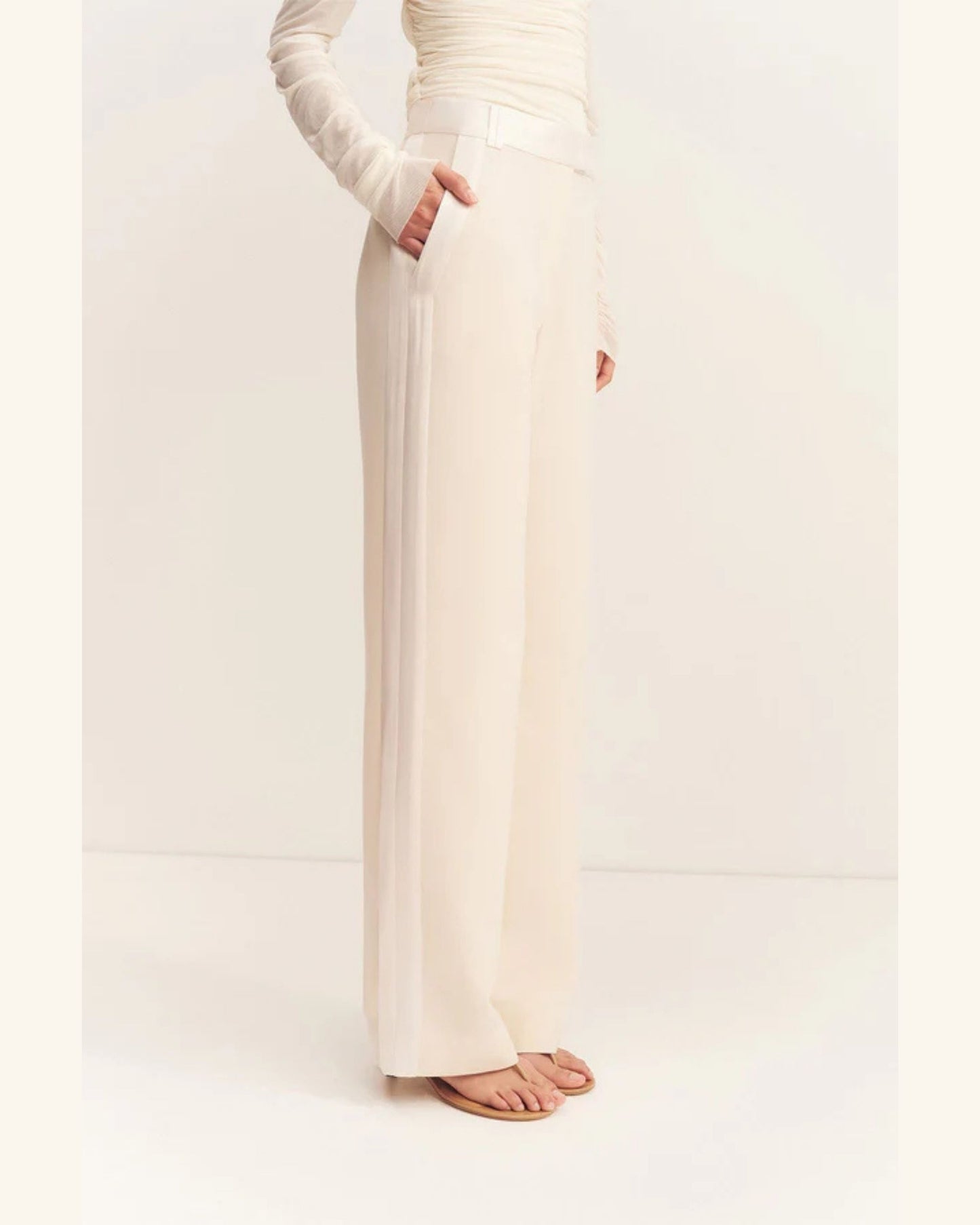Side view, Adri Tuxedo Side Panel Pants with a contrast satin waistband, side panels, and pockets. Features include a mid-rise fit, knife pleats, jet pockets, and a relaxed straight leg. Available at Georgette bridal boutique in Brussels and online at georgettebridal.com.