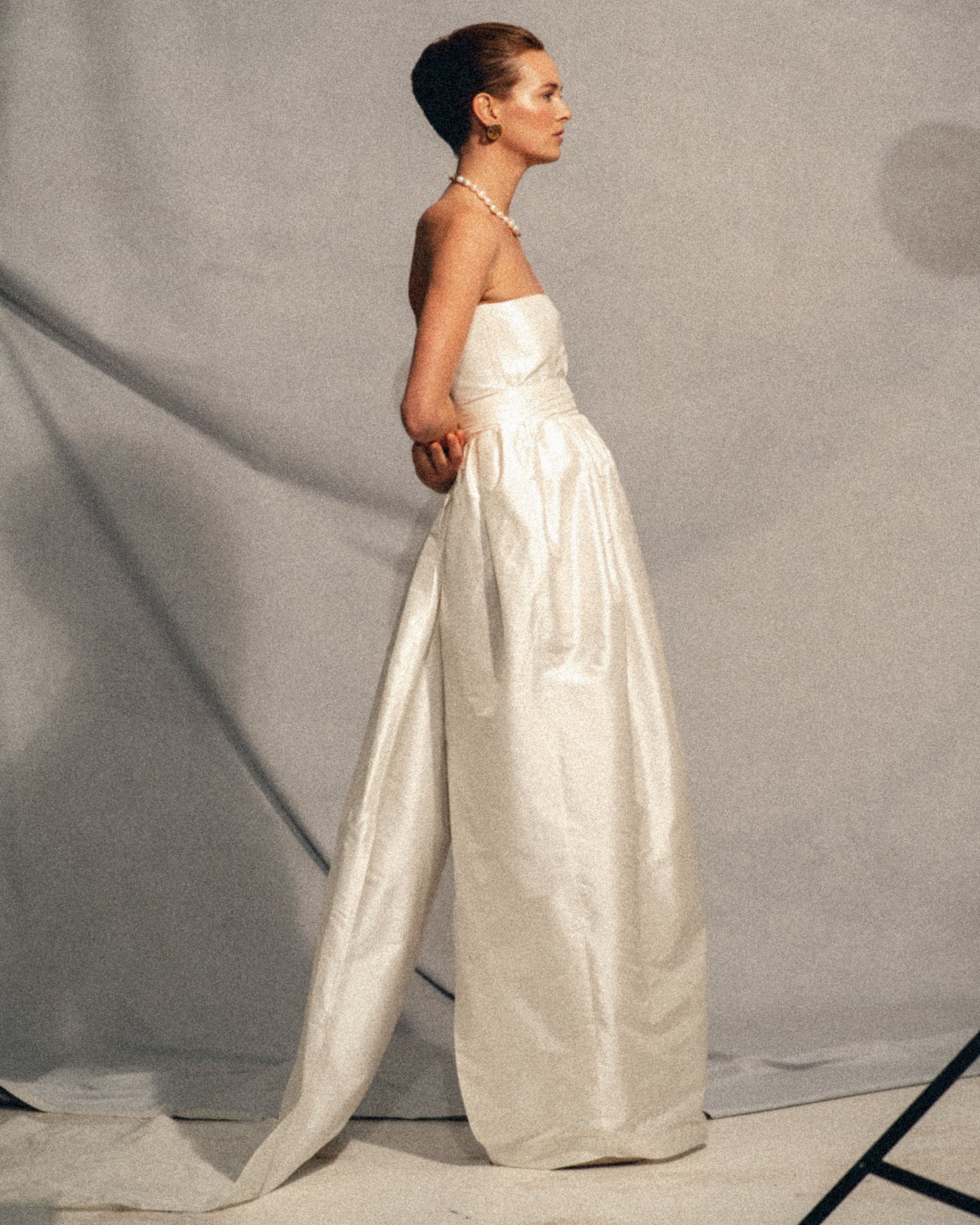 Side view of the Cece wedding gown with a tulip-shaped silk skirt, structured bustier, refined belt, and removable train, handmade in Amsterdam, available at Georgette bridal boutique in Brussels and online at georgettebridal.com.