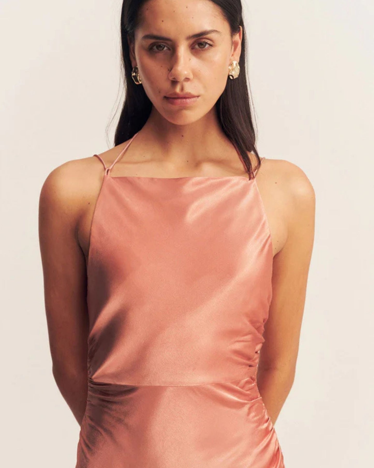 Close-up an antique rose satin maxi dress with a square high neckline, halter tie, ruched waist, and low open back. Made from sustainable LENZING™ ECOVERO™ viscose. Available at Georgette bridal boutique in Brussels and online at georgettebridal.com.