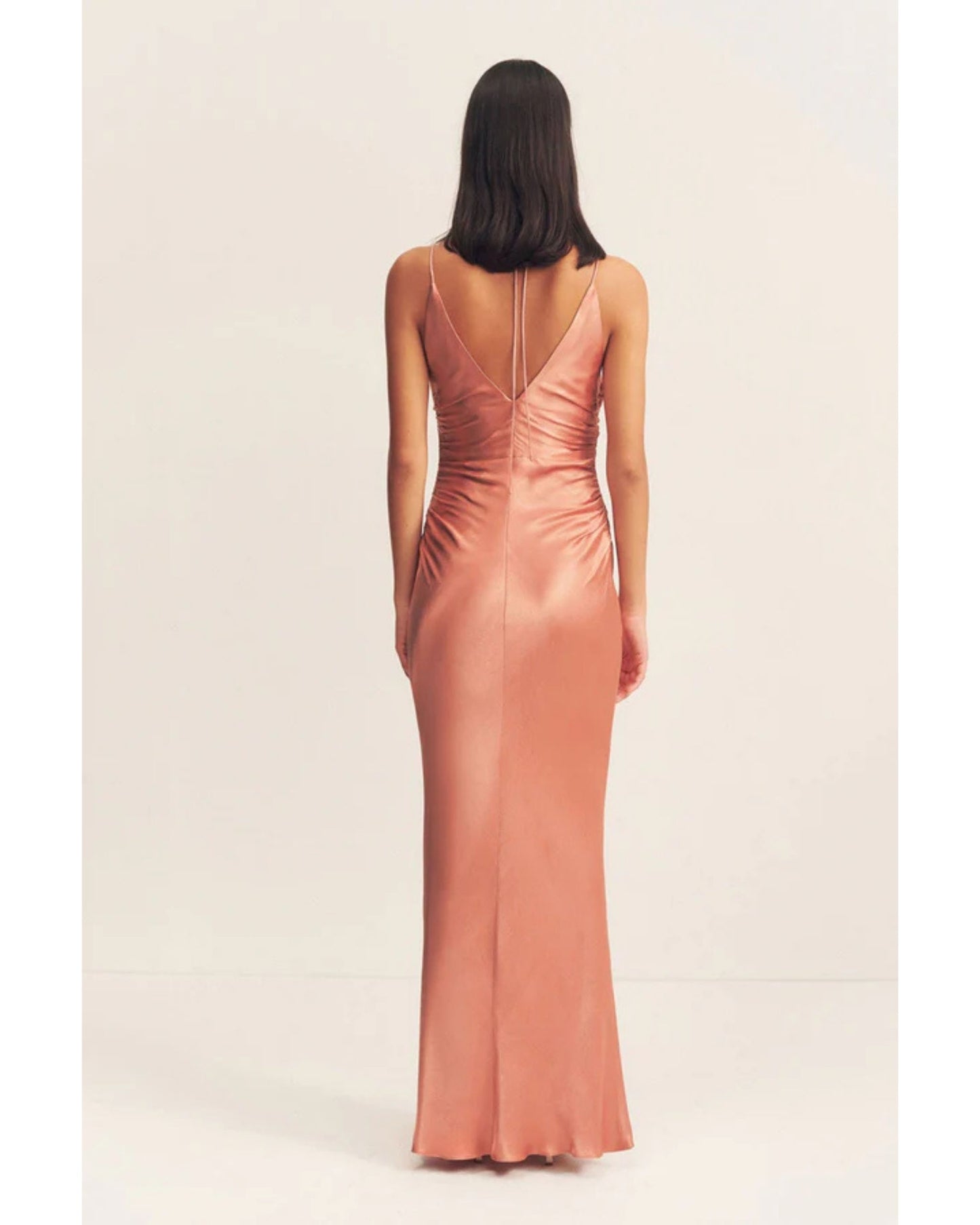 Back view of model wearing an antique rose satin maxi dress with a square high neckline, halter tie, ruched waist, and low open back. Made from sustainable LENZING™ ECOVERO™ viscose. Available at Georgette bridal boutique in Brussels and online at georgettebridal.com.
