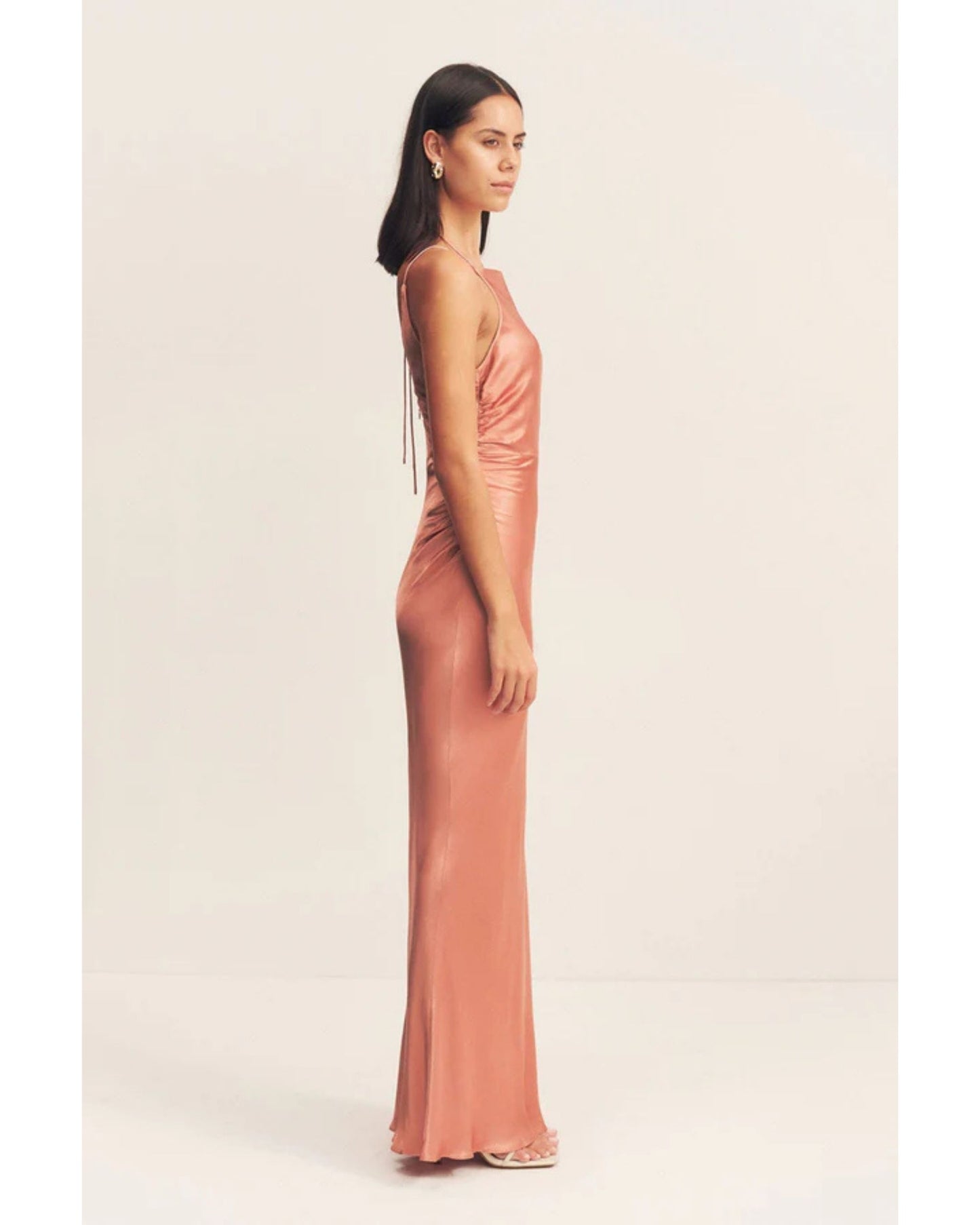 Side view of an antique rose satin maxi dress with a square high neckline, halter tie, ruched waist, and low open back. Made from sustainable LENZING™ ECOVERO™ viscose. Available at Georgette bridal boutique in Brussels and online at georgettebridal.com.