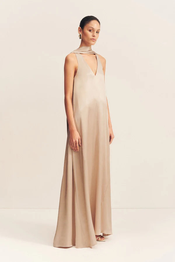 An elegant golden maxi dress with a deep plunging neckline and draped scarf detail, made from satin-finish LENZING™ ECOVERO™ viscose for a sophisticated, fluid look. Available at Georgette bridal boutique in Brussels and online at georgettebridal.com.