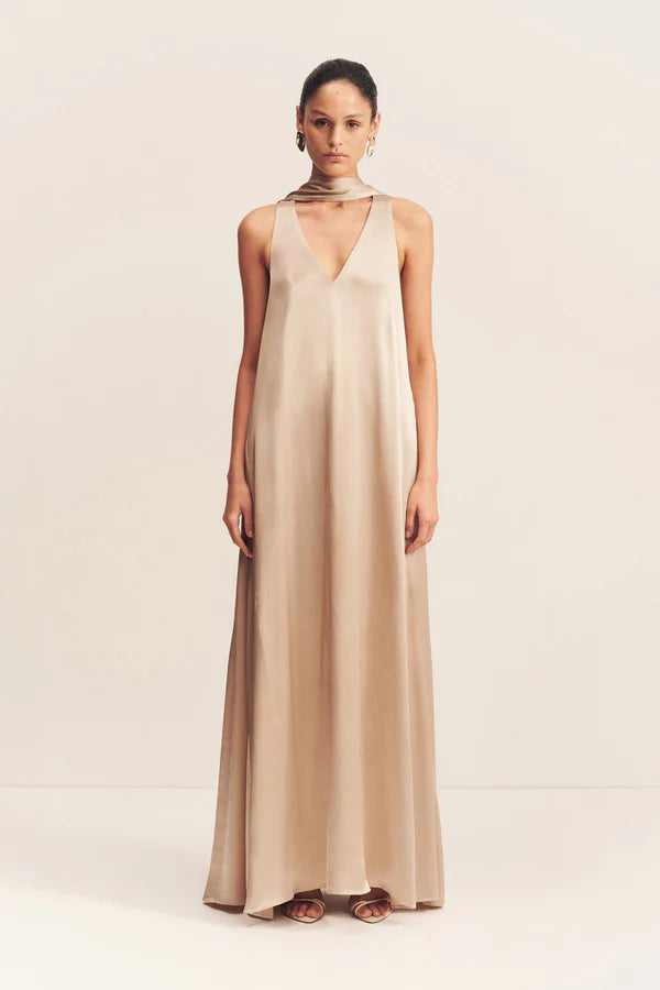 Model wearing an elegant golden maxi dress with a deep plunging neckline and draped scarf detail, made from satin-finish LENZING™ ECOVERO™ viscose for a sophisticated, fluid look. Available at Georgette bridal boutique in Brussels and online at georgettebridal.com.