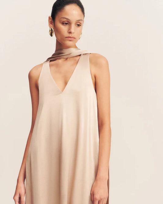 Model wearing an elegant golden maxi dress with a deep plunging neckline and draped scarf detail, made from satin-finish LENZING™ ECOVERO™ viscose for a sophisticated, fluid look. Available at Georgette bridal boutique in Brussels and online at georgettebridal.com.