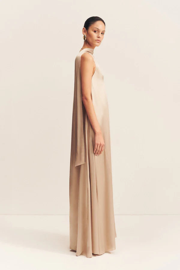 Side view, elegant golden maxi dress with a deep plunging neckline and draped scarf detail, made from satin-finish LENZING™ ECOVERO™ viscose for a sophisticated, fluid look. Available at Georgette bridal boutique in Brussels and online at georgettebridal.com.