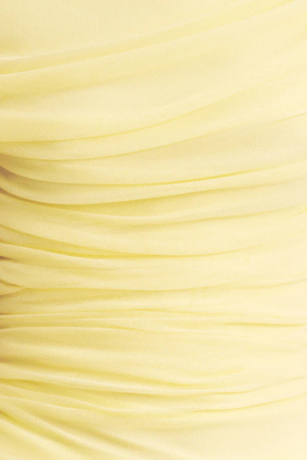 Fabric focus, asymmetrical yellow one-shoulder maxi dress featuring sheer mesh and delicate lace contrast, gathered details, and a flowing lace skirt with a subtle back split. Available at Georgette bridal boutique in Brussels and online at georgettebridal.com.