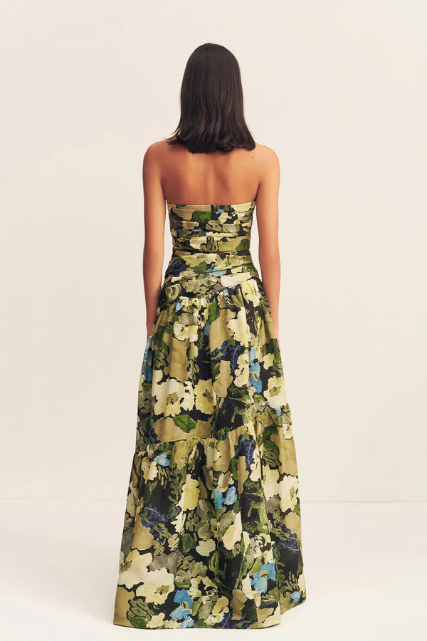 Back view of a strapless tiered maxi dress in a sheer Botanical Floral print, featuring a softly draped asymmetrical bodice, full tiered skirt, and invisible side zip. Crafted from a linen and TENCEL™ blend. Available at Georgette bridal boutique in Brussels and online at georgettebridal.com.