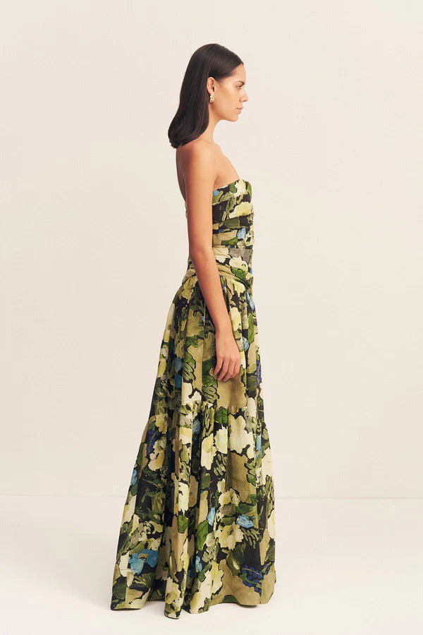 Side view of a strapless tiered maxi dress in a sheer Botanical Floral print, featuring a softly draped asymmetrical bodice, full tiered skirt, and invisible side zip. Crafted from a linen and TENCEL™ blend. Available at Georgette bridal boutique in Brussels and online at georgettebridal.com.