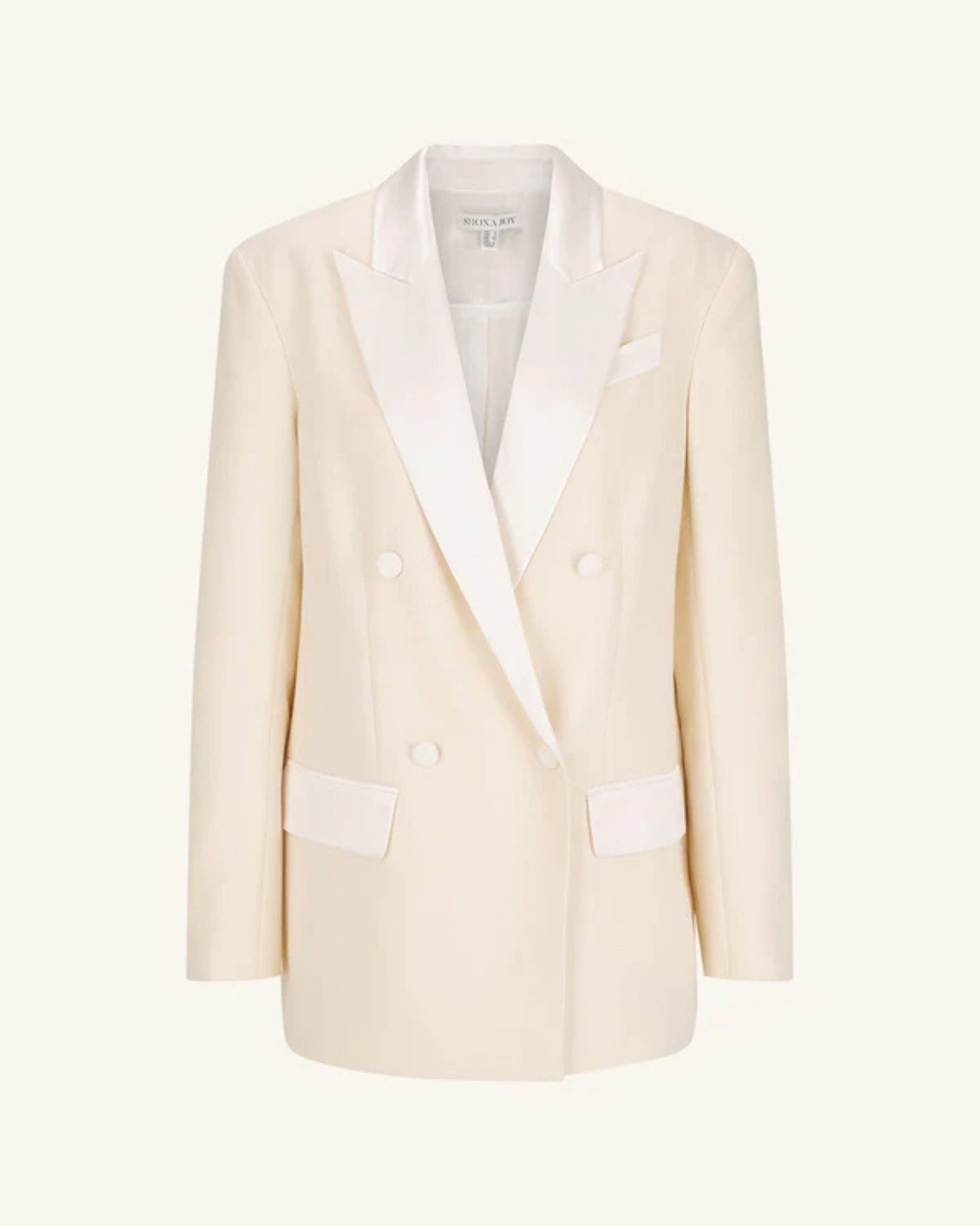 Product shot, a double-breasted blazer in soft rice with contrast satin lapel, collar, and flap pockets. Features tailored sleeves, back vent, and structured silhouette. Available at Georgette bridal boutique in Brussels and online at georgettebridal.com.