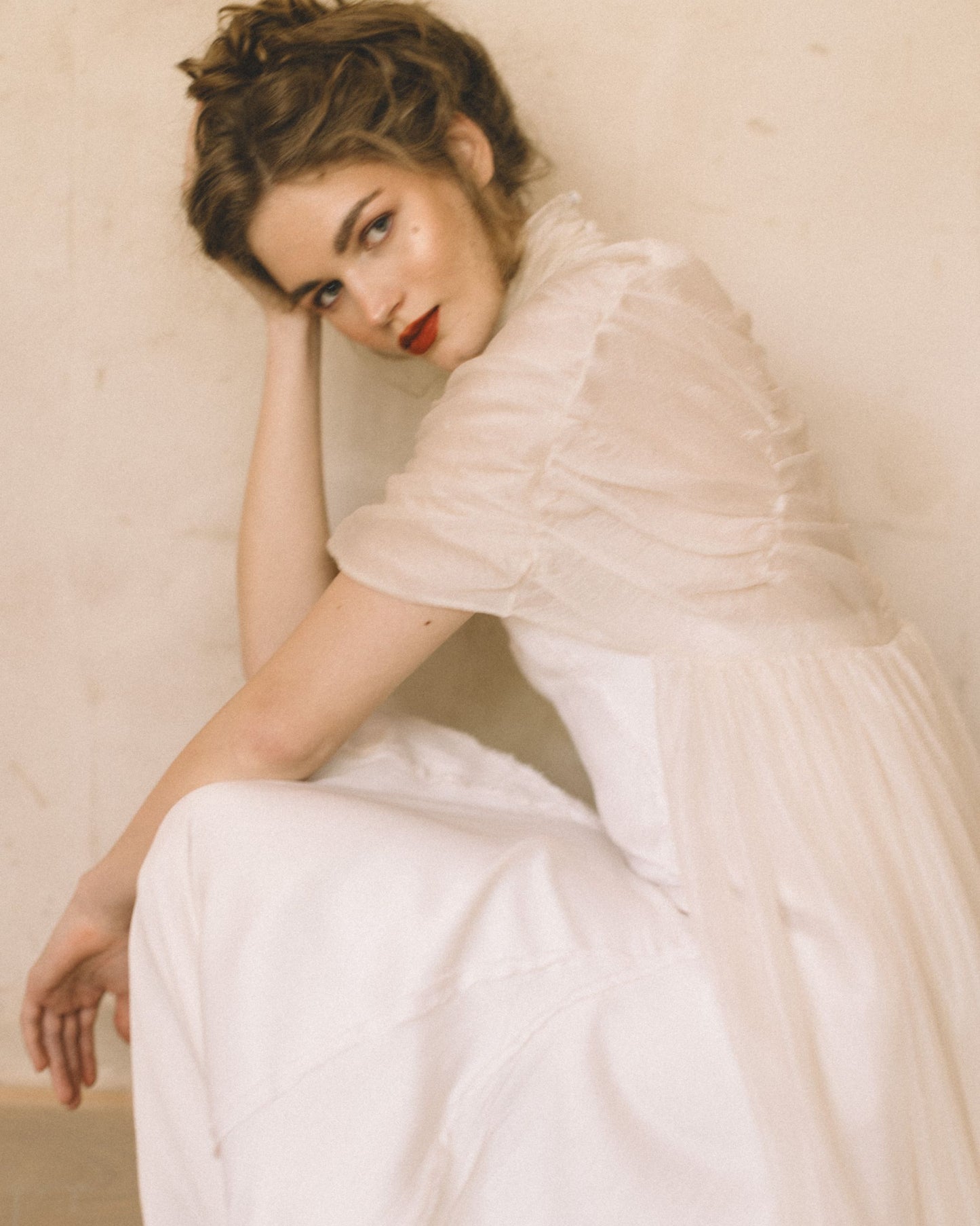 Model wearing the Elise Silk Cape by The Muse Collective pictured seated against a beige wall