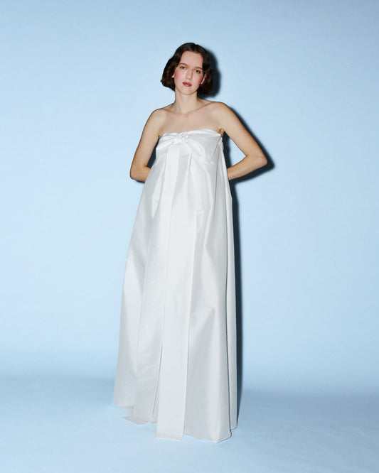 Model wearing the Estelle Wedding Dress With Bow, featuring a straight neckline, delicate removable straps, and a signature front bow. Crafted from crisp taffeta for a timeless and elegant bridal look. Available at Georgette bridal boutique in Brussels and online at georgettebridal.com.