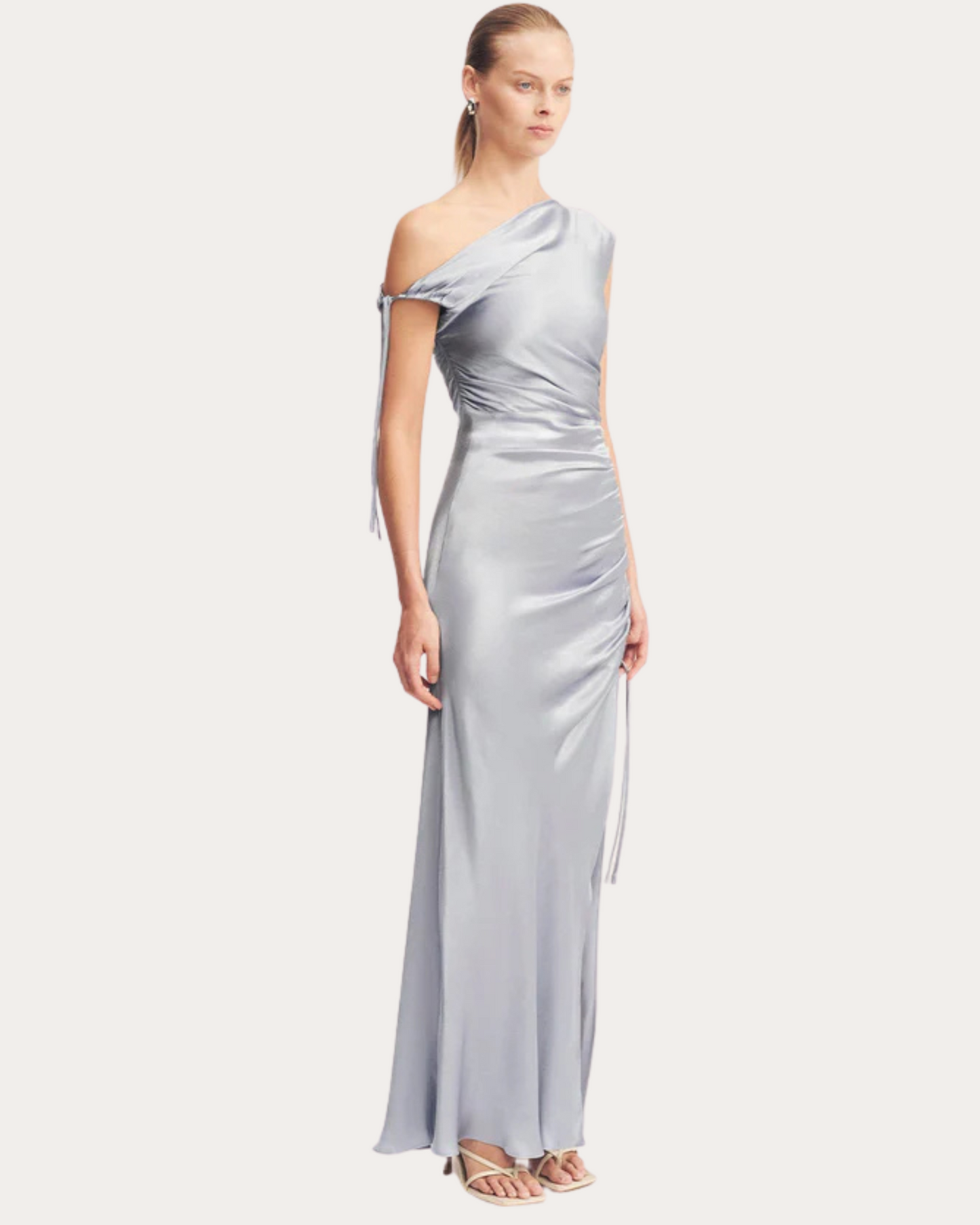 Three-quarter view of the powder blue La Lune One-Shoulder Dress with gathered waist and side tie detail, available at Georgette Bridal in Brussels.