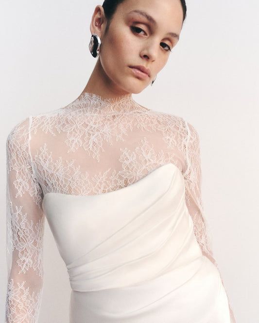 Model wearing the Lambent Lace Long Sleeve Bridal Bodysuit with intricate lace detailing and a high neckline, offering a timeless and sophisticated bridal look. Available at Georgette bridal boutique in Brussels and online at georgettebridal.com.