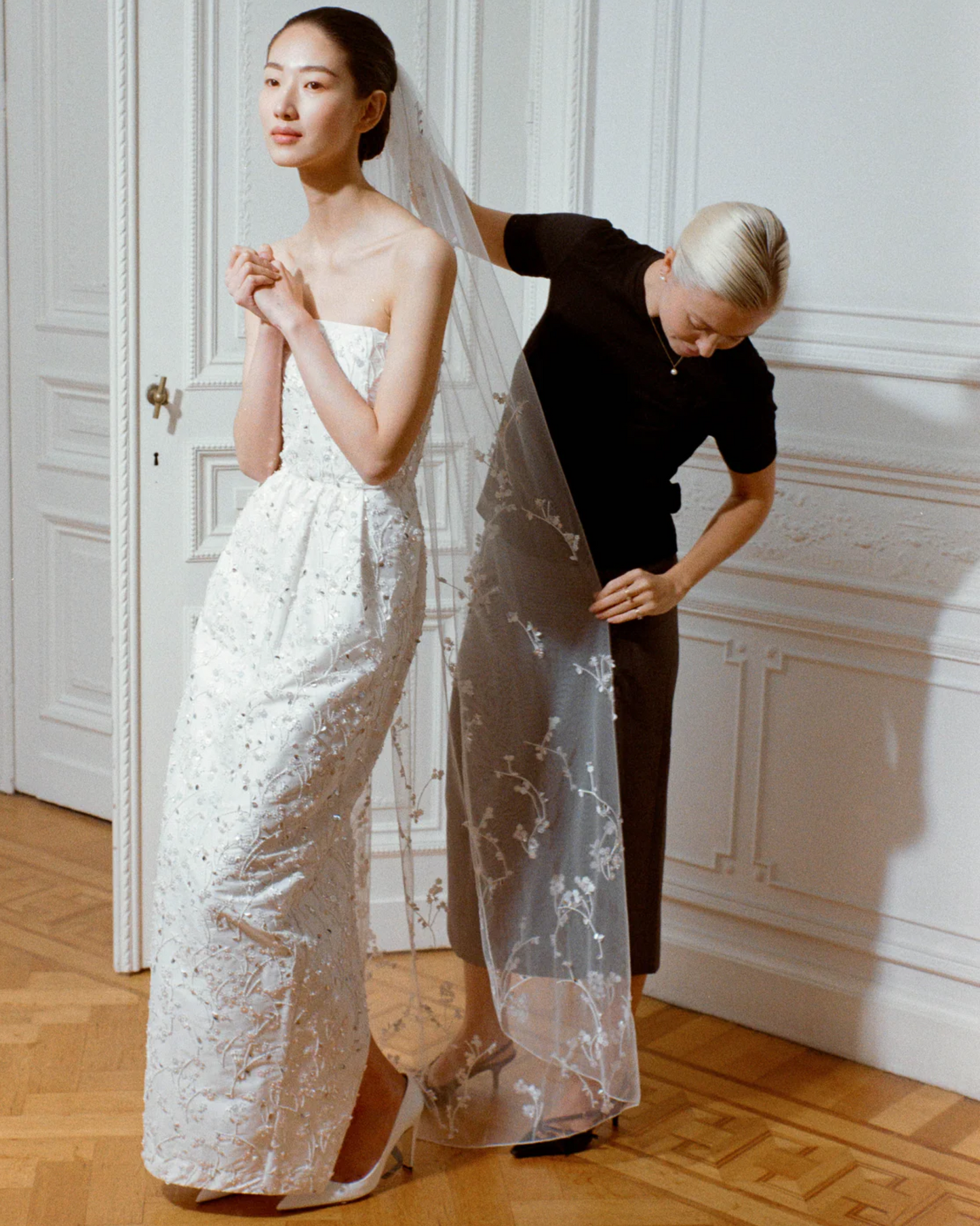 Bride being styled with the Bernadette Little Flower bridal veil, available at Georgette bridal boutique in Brussels. The veil’s length and intricate detailing are beautifully visible.