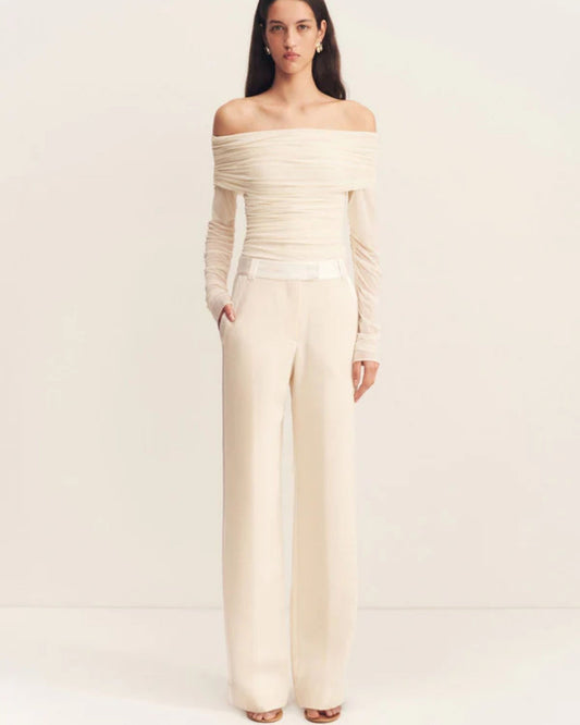 Model wearing the Mira Long Sleeve Off Shoulder Top in ivory - a sheer mesh top with an off-shoulder neckline, long gathered sleeves, and ruched side seams, creating a sculpted, elegant silhouette, available at Georgette bridal boutique in Brussels and online at georgettebridal.com.