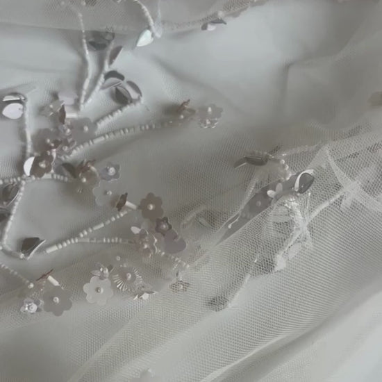 Zoom-in on the floral embroidery of the Bernadette Little Flower veil, available at Georgette. The video captures the fine silver thread and hand-applied flowers on soft ivory tulle.