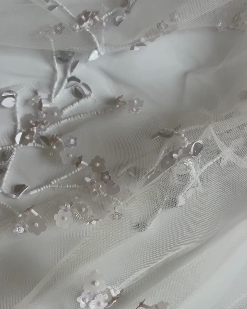 Zoom-in on the floral embroidery of the Bernadette Little Flower veil, available at Georgette. The video captures the fine silver thread and hand-applied flowers on soft ivory tulle.